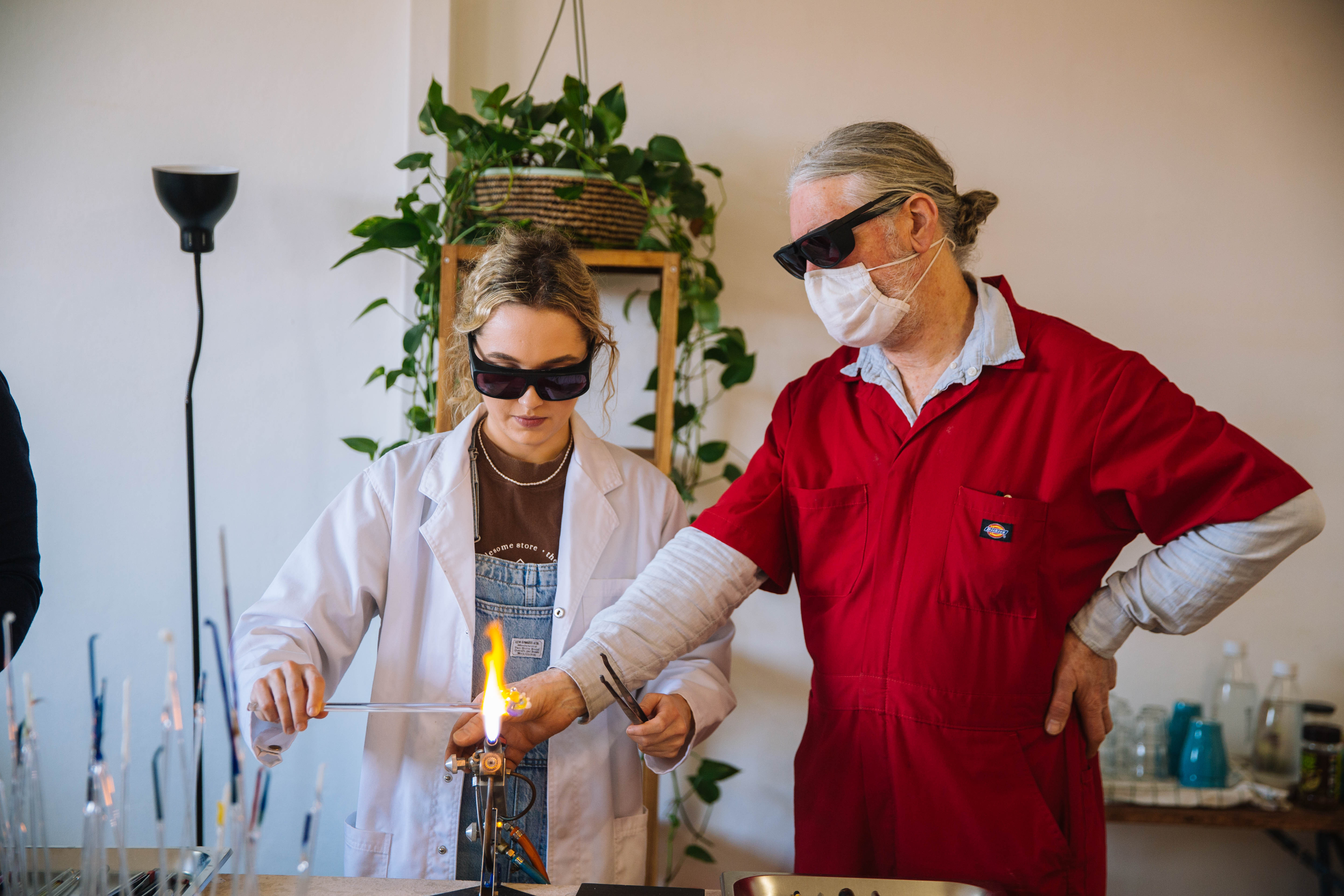 A teacher showing a student how to shape glass over a flame